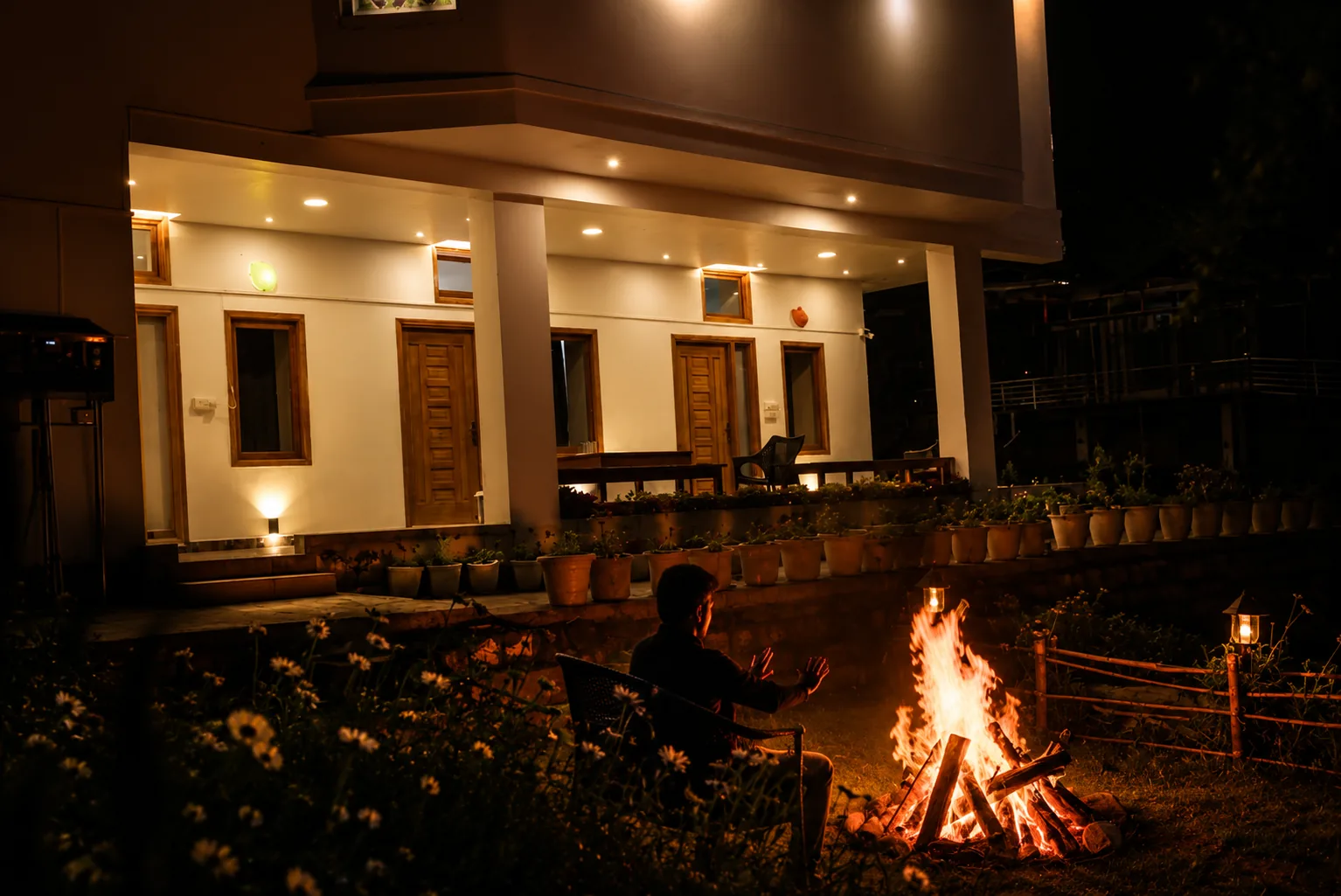 A guest sitting at the bonfire at night with the lit verandah behind