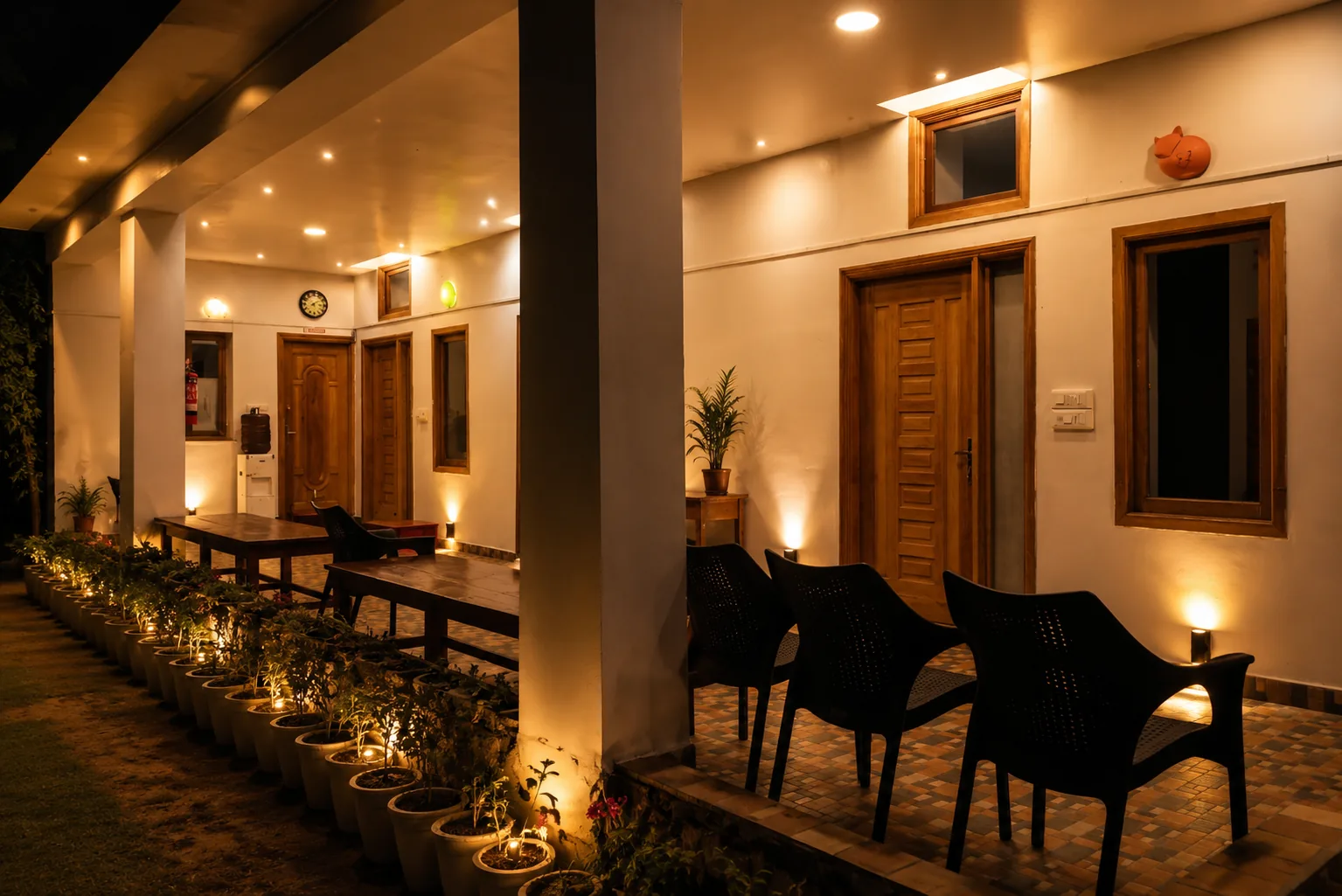 Long lit verandah with wooden communal tables and rows of potted plants